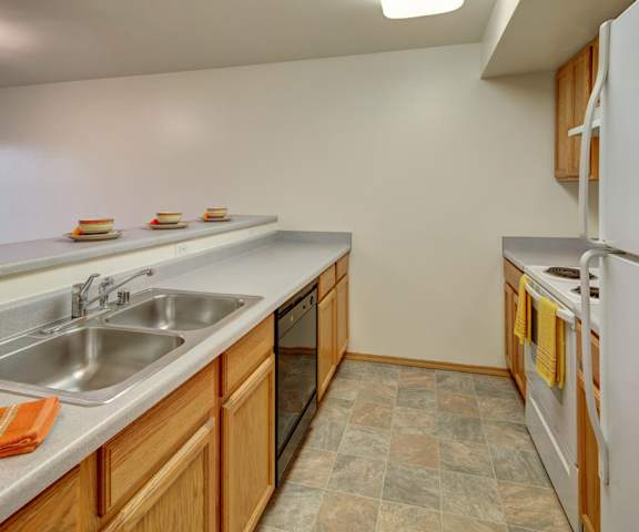 The cozy kitchen with spacious gray counters, a white refrigerator, a black dishwasher, and a white oven with light wooden cabinets with a lot of room at Strawberry Lane Apartment Homes. 