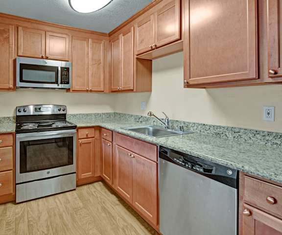 A large, modern kitchen with stainless steel appliances, bar counter, granite countertops with lots of room, and large wooden cabinets at the Club at Eagle Point Apartment Homes. 