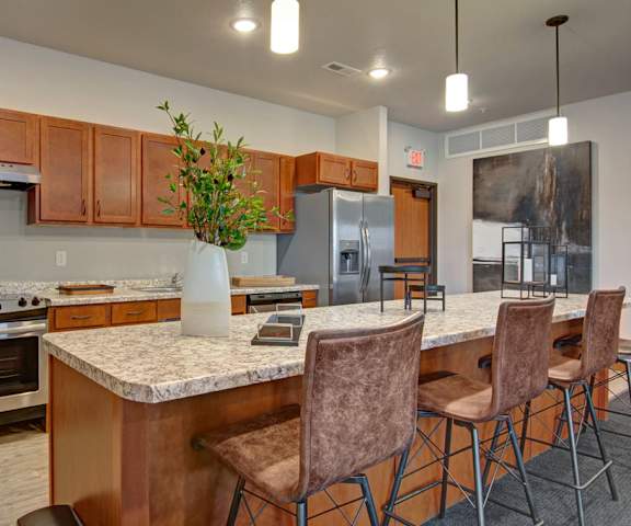 A large, modern kitchen with stainless steel appliances, bar counter with barstools, kitchen utensils, marble countertops with lots of room, and large wooden cabinets at the Club at Heritage Apartment Homes. 