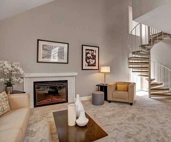 The amazing  gray and white resident lounge with a fireplace, couches, decorations, spiral staircase leading to the upstairs, plush chairs, and coffee tables at the Cove Apartment Homes. 