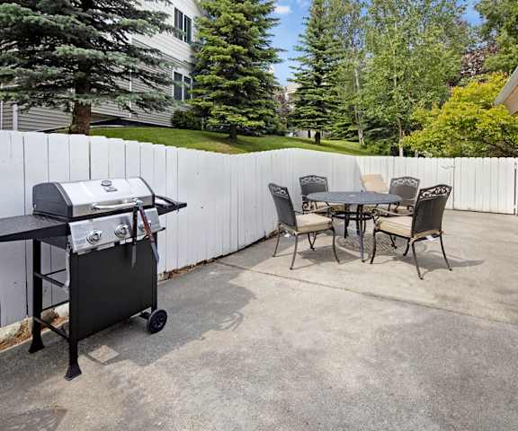 An outdoor resident patio with a grill area and tables and chairs surrounded by white fences and the apartment buildings at the Highlands Luxury Residences. 