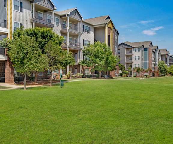 The exterior of the apartments and the green space with grass, trees, and shrubs at Lincoln at Central Park Apartment Homes. 