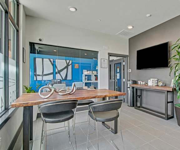 The front office and resident lounge with a table and chairs, couches, a TV, plants, a coffee station, and a coffee table at Vive Apartment Homes. 