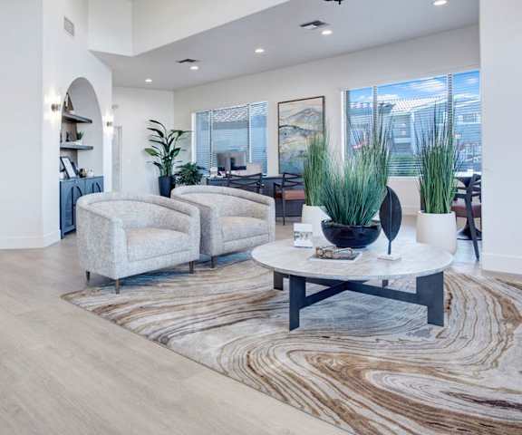 The front office and resident lounge with large windows showing the skyline, cozy couches and plush chairs, a TV, and a coffee table at Pala Mesa Apartments. 