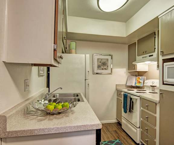 A cozy kitchen with white appliances, a light counter with lots of room, and spacious wooden cabinets at Paradise Falls Apartments. 