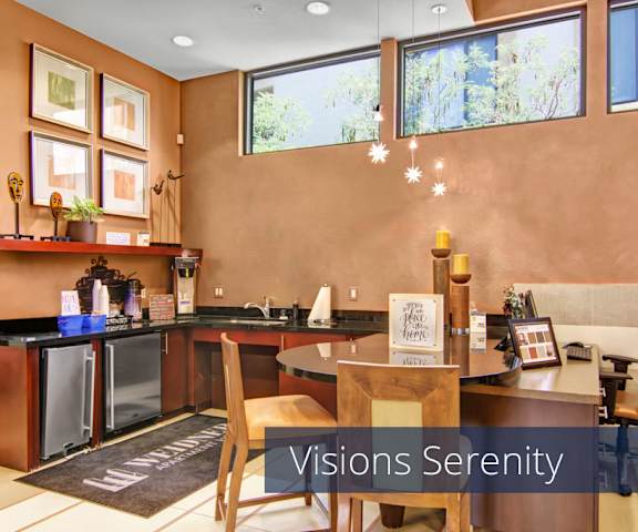 The modern resident lounge with a kitchen with stainless steel appliances, a coffee station, wall art, and a table and chairs at Visions Apartment Homes. 