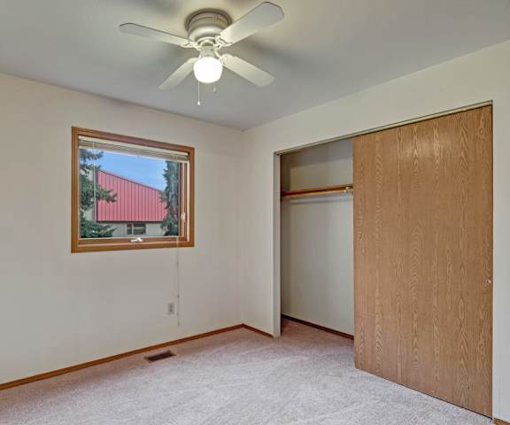A large, empty carpeted bedroom with overhead lighting, a closet, and a window at Wildwood Estates Apartment Homes. 