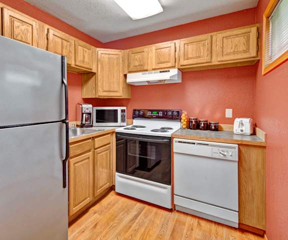 A cozy kitchen with white appliances, light counter, and large wooden cabinets at Wildwood Estates Apartment Homes. 
