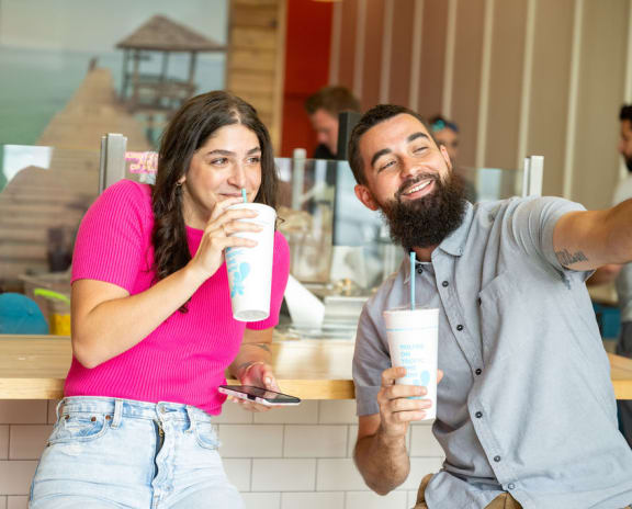 a man and a woman standing in front of a counter holding drinks and a phone