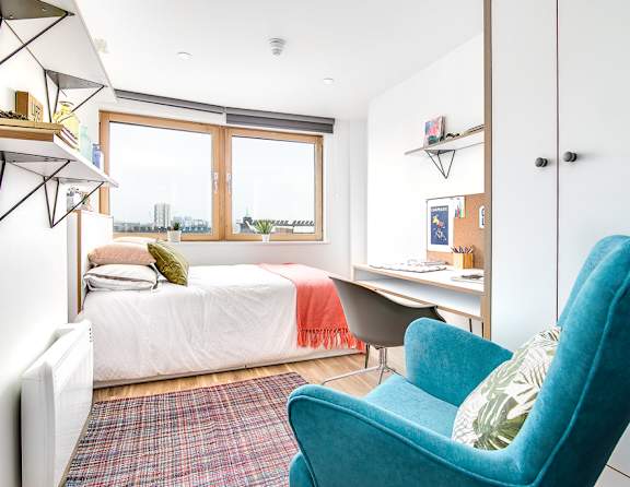 A blue chair sits in a white room with a bed and desk.