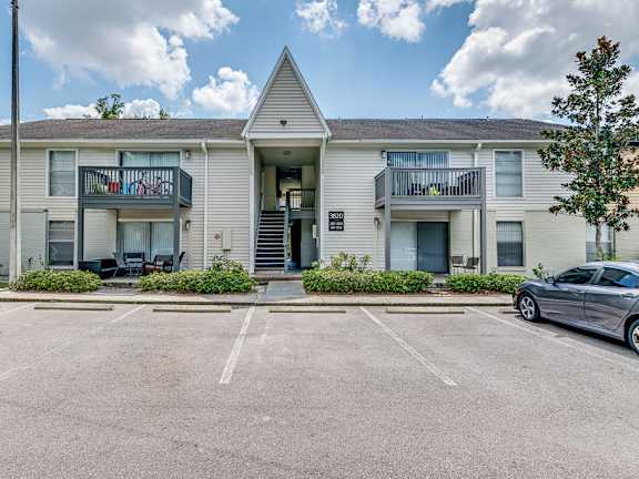 A car is parked in a parking lot in front of a two-story apartment building.