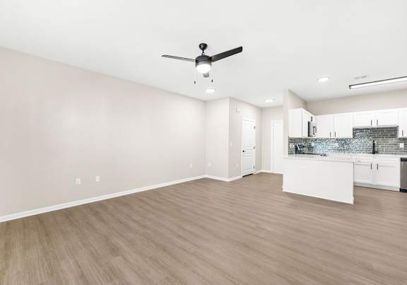 A room with a ceiling fan and a kitchen area in the background.