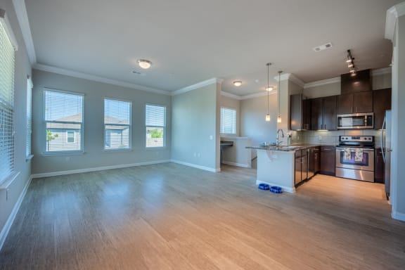 Living room with hardwood flooring facing kitchen with stainless steel appliances