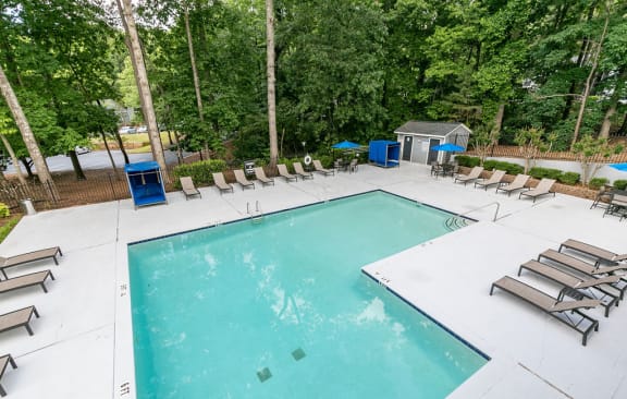 a swimming pool with chaise lounges and chairs in a backyard with trees  at The Atlantic Howell Station, Duluth, GA