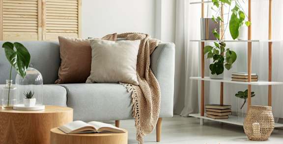 A living room with a grey couch, a wooden table, and a plant on the shelf.