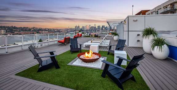 A rooftop patio with a fire pit and chairs overlooking a city skyline at dusk. at The Summit at Lake Union, Seattle, WA