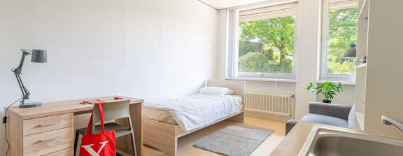 A bedroom with a bed, desk, and window.