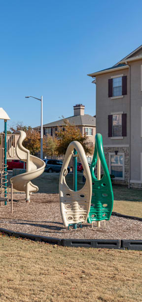 A playground with a green slide and a white swing set.