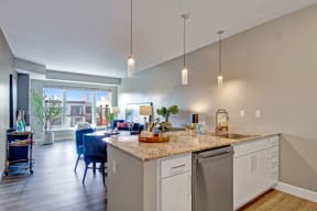 A kitchen with white cabinets and marble countertops and a view of the dining room and the living room at Gatsby Apartments. 