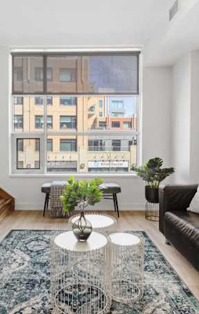 A living room with a black couch, a television, and a large window.