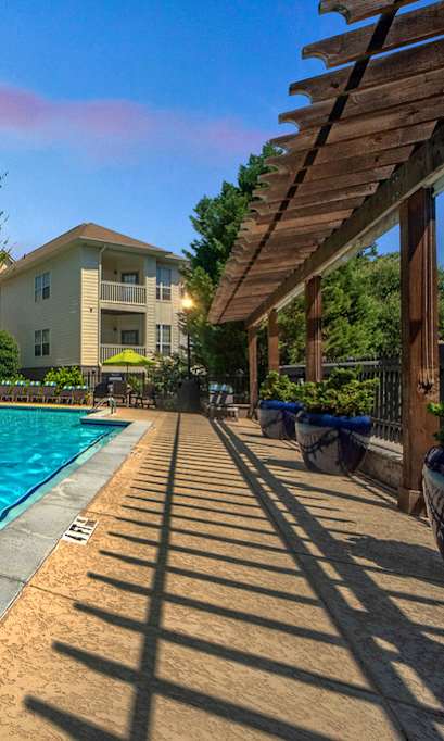 A large swimming pool in front of a house with a wooden pergola.