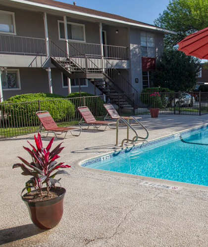 A red umbrella is next to a table and chairs by a pool.