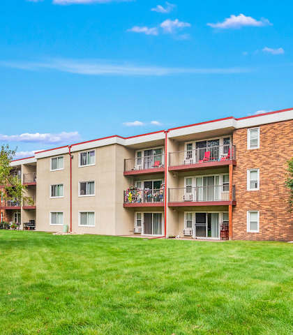 A red brick apartment building with a green lawn in front.
