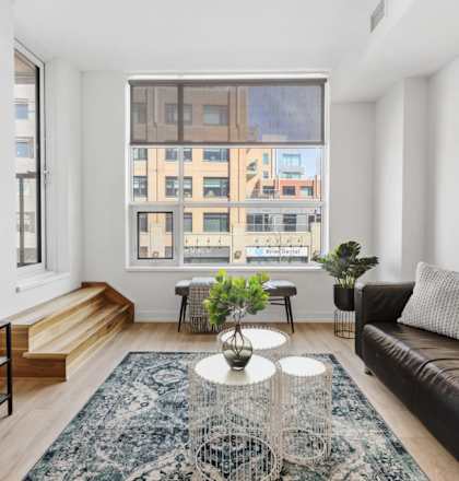 A living room with a black couch, a television, and a large window.