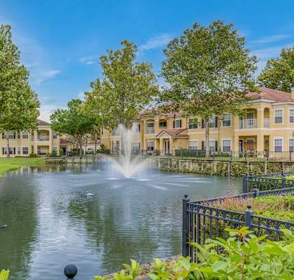 A fountain in the middle of a pond in front of apartment buildings.