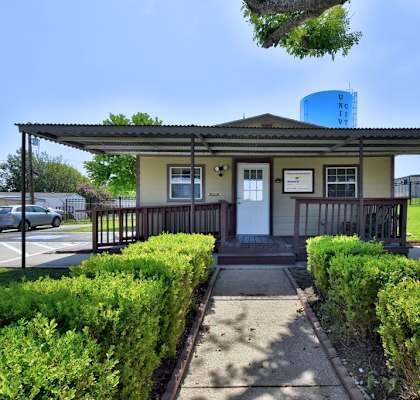 a small yellow building with a porch and a walkway in front of it at Buckingham Village in Universal City, TX