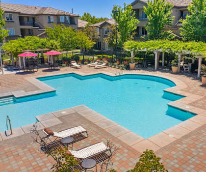 A turqouise swimming pool with chairs and umbrellas in front of the Artisan 8282 building. 