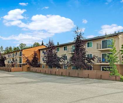 The exterior of the apartment buildings showing the tan buildings with balconies, trees surrounding them, and the parking lot at Quiet Creek Apartment Homes. 