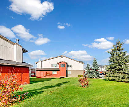 The bright exterior of Strawberry Lane Apartment Homes with grassy fields and trees surrounding the white, tan and red homes. 