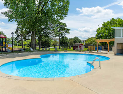 A round blue swimming pool surrounded by a concrete patio and a playground.