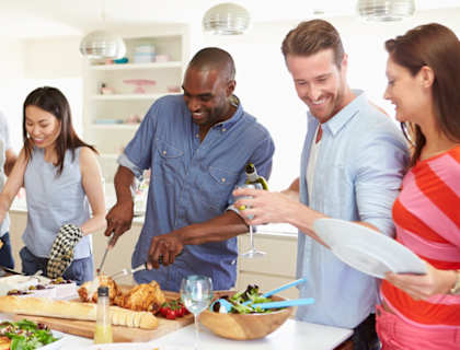 A group of people are gathered around a table, preparing and enjoying a meal together.