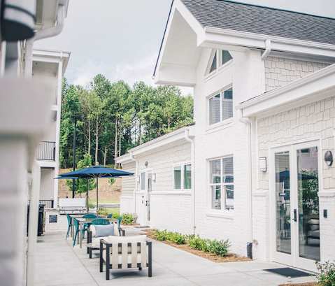 the patio of a white house with tables and chairs at Woodlands Creekside Apartments, McDonough, GA, 30253