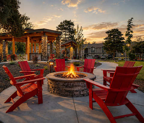 A fire pit surrounded by red chairs in a garden.