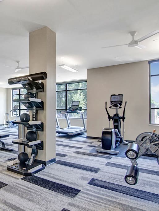 A gym with cardio machines, TVs, and weights at Gatsby Apartments. 