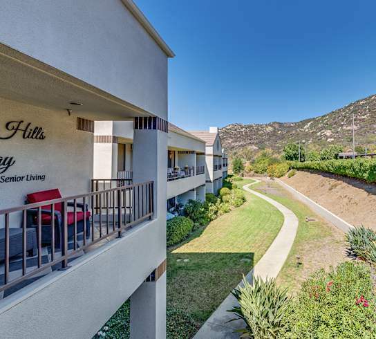 A view of a balcony overlooking a pathway and a grassy area with a sign that says  at Legacy Hills at Poway 55+ Apartments, California