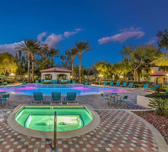 a large swimming pool with chairs and a jacuzzi at night at Mirasol Apartments, Las Vegas, NV