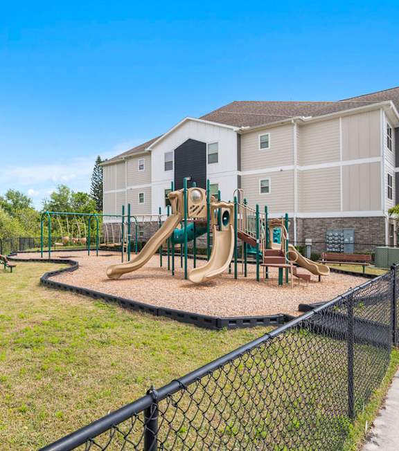 A playground with a green fence and a yellow slide at Mode at Melbourne, LLC Apartments, Melbourne, Florida