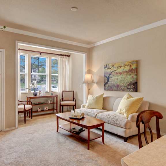 The spacious living room with a white couch, yellow throw pillows, large windows, wall art, two white chairs by the window, coffee table, and decorations at Stoneleigh at the Reserve Apartment Homes. 