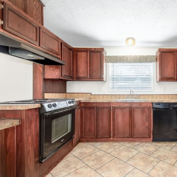 a kitchen with wooden cabinets and a black refrigerator at Buckingham Village in Universal City, TX