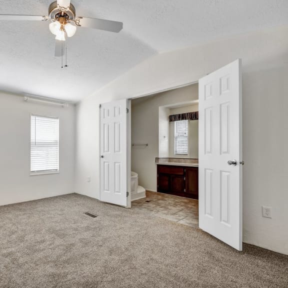 a bedroom with a ceiling fan and a bathroom in the background at Buckingham Village in Universal City, TX