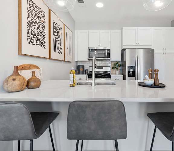 A modern kitchen with white cabinets and a large island with chairs at Madison Prickett Preserve, Yardley