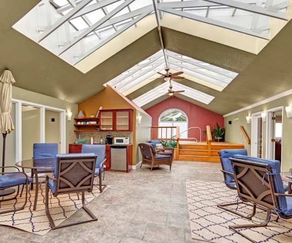 An amazing resident lounge with skylights with light streaming in, tables, warm blue chairs, a kitchenette with a coffee machine, dishwasher, and microwave, and ceiling fans at the Club at Eagle Point Apartment Homes. 