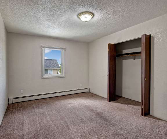 A large, empty carpeted bedroom with overhead lighting, a window, and a closet at the Greenbriar Apartment Homes. 