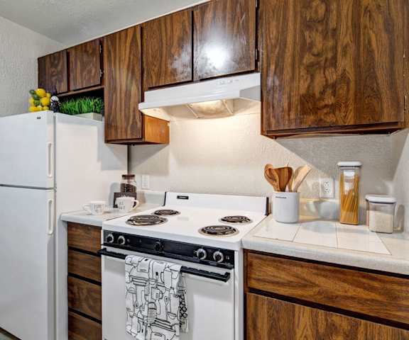 A cozy kitchen with white appliances, kitchen utensils, overhead lighting, light countertops with lots of room, and large wooden cabinets at the Greenbriar Apartment Homes. 