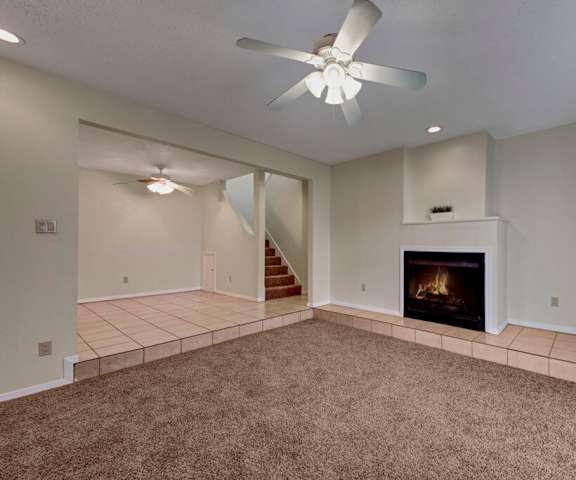 An empty living room with carpeting and the stairs at Las Colinas Apartments. 