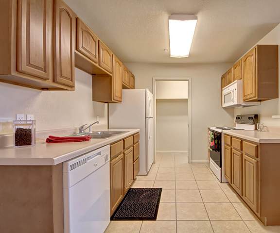 A cozy kitchen with white appliances, light counter, and spacious wooden cabinets at Lexington Court Apartment Homes. 